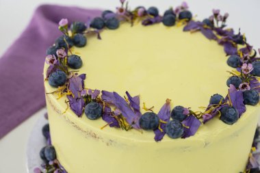 Çiçek desenli limonlu yaban mersinli kek, yaban mersinli açık sarı krema ve peçeteli çiçekli süslemeli, kutlama için mükemmel bir kafe zarif pastası.