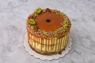 Fıstıklı Karamelli Drip Pastası 'nda bol karamel serpiştirilmiş, üzeri şam fıstıklı ve fındıklı gri arka planda pişmiş kafe tatlısının fındıklı yarısı.