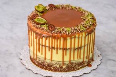 Fıstıklı Karamelli Drip Pastası 'na zengin karamel serpiştirilmiş, üzerinde şam fıstığı ve fındıklı fındıklı gri arka plan manzaralı fırında pişmiş tatlı katmanları