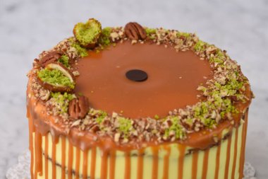 Fıstıklı Karamelli Drip Pastası 'nda bol karamel serpiştirilmiş, üzerinde şam fıstığı ve fındıklı, gri arka planda yakın planda kalan fındıklı, fırında pişirilmiş tatlıların yan görüntüsü yer alıyor.