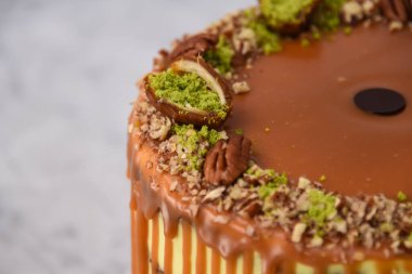 Fıstıklı Karamelli Drip Pastası 'nda zengin karamel serpiştirilmiş, üzerinde şam fıstığı ve fındıklı, gri arka planda yakın plan, fırında pişirilmiş tatlı manzarası.