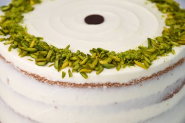 Zarif Pistachio Pastası Görünür pasta katmanları ve kenarlarında doğranmış şam fıstığı ile süslenmiş pürüzsüz beyaz krema lezzetli tatlı için arka planda yakın plan görüntüsü