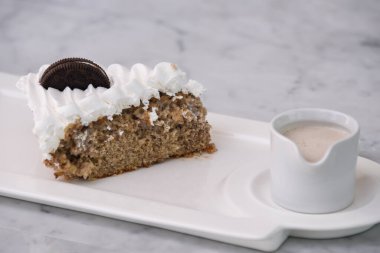 Kremalı bisküvi dilimlenmiş ezilmiş çikolatalı sandviç kurabiyeleri üzerine beyaz krema ve süt sosu katılmış arka planda izole edilmiş olarak servis edilen tabakta servis edilen hoşgörülü tatlı.