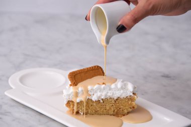 Kurabiyelerin üzerine süt dökülüyor Biscoff Tres Süt soslu kek dilimi tepside servis edilen yumuşacık kremayla klasik hoşgörülü tatlı arka planında izole edilmiş