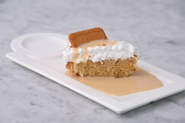 Biscoff Tres Leches Pastası Süt Sosu ile dilimlenmiş krema tepside servis ediliyor. Gri arka plan görünümlü hoş bir tatlı.