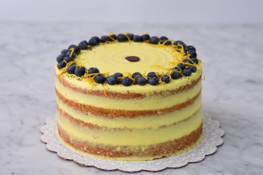 Zarif Limonlu Yaban mersinli Kek canlı sarı limonlu krema ve taze yaban mersinli süsleme, limon aromalı ve haşhaş tohumlu gri arka plan manzaralı fırında pişmiş tatlı.