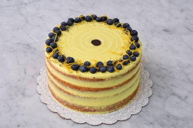 Zarif Limonlu Yaban mersinli Kek canlı sarı limonlu krema ve taze yaban mersinli süs, limon aromalı ve haşhaş tohumlu süslemeli gri arkaplan manzaralı fırın tatlı.