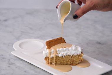 Kurabiyelerin üzerine süt dökülüyor Biscoff Tres Sülükleri Süt Sosu ile dilimlenmiş yumuşak krema tepside servis ediliyor Gri arka plan yakın plan görüntüsü klasik ve hoşgörülü tatlı