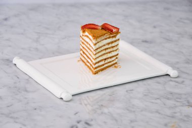 Klasik Medovik Bal Katmanı. Bal süngeri katmanları ve çilek dilimleriyle kaplı kremalı tablalar. Gri arka plan görünümlü klasik kafe tatlısına ayrılmış tepside servis ediliyor.