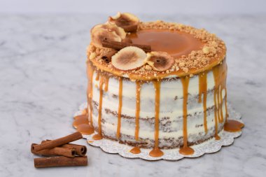 Karamel, incir dilimleri, tarçın ve kavrulmuş fındıklar ile kaplanmış, arkaplanda yakın planda kalan fırında pişmiş tatlı manzaralı nemli kek katmanları serpiştirilmiş.