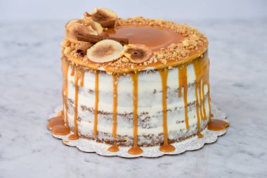 Zarif Karamel İncirli Drip Pastası 'nda zengin karamel serpiştirilmiş, üzerinde kurutulmuş incir dilimleri ve arka planda izole edilmiş doğranmış fındıklar ve fırınlanmış kahve tatlısının yakın plan görüntüsü yer alıyor.