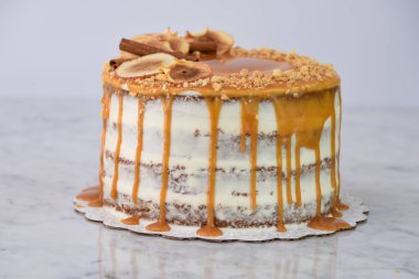 Zarif Karamel İncirli Drip Pastası 'nda zengin karamel serpiştirilmiş, üzerinde kuru incir dilimleri olan nemli pasta katmanları ve gri arka planda izole edilmiş fındıklar pişmiş kafe tatlı manzarası.