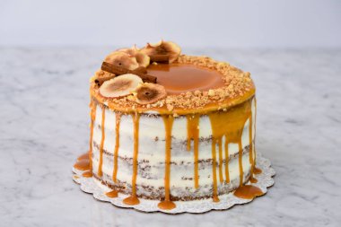 Karamel İncirli Drip Pastası 'nda zengin karamel serpiştirilmiş, üzerinde kuru incir dilimleri olan nemli pasta katmanları ve fırında pişmiş tatlıların arka planında izole edilmiş fındıklar var.