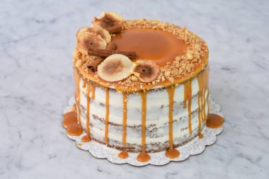 Zarif Karamel İncirli Drip Keki 'nin içeriğinde zengin karamel serpiştirilmiş, üzerinde kurutulmuş incir dilimleri ve arka planda izole edilmiş fındıklar var.