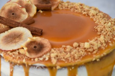 Zarif Karamel İncirli Drip Pastası 'nda zengin karamel katmanları serpiştirilmiş, üzerinde kuru incir dilimleri ve gri arka planda izole edilmiş doğranmış fındıklar var.