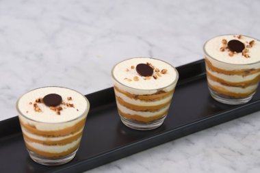 Klasik Tiramisu Tatlısı berrak bardaklarda kahve katmanları, kremşantili mascarpone ve üzerine krem şanti sürülmüş kakao ve doğranmış fındıklar İtalyan tatlısına yakından bakıyor.