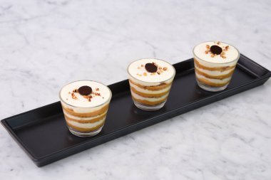 Klasik Tiramisu Tatlısı berrak bardaklarda kahve katmanları sergileniyor kremalı mascarpone, krem şantili toz kakao ve İtalyan tatlısına ait fındık ezmesi.