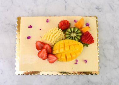 Çilek, mango, kivi ve anananaslı tropikal meyveli, zarif Pistachio Katmanı Keki ve leziz bir tatlı manzarası var.