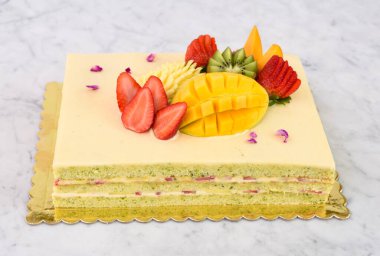 Çilek, mango, kivi ve anananas dahil olmak üzere tropikal meyveli Şam fıstıklı kek ve lezzetli tatlı kekinin narin gül yaprakları manzarası.