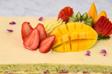 Çilek, mango, kivi ve anananasın yanı sıra narin gül yapraklarıyla birlikte tropikal meyveli bir pasta.