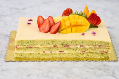 Çilek, mango, kivi ve anananasın yanı sıra aromalı tatlı için narin gül yaprakları manzaralı zarif Pistachio Keki.