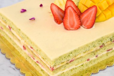 Çilek, mango, kivi ve ananas dahil olmak üzere tropikal meyveli, zarif Pistachio Katmanı Keki ve lezzetli kafe tatlı kekinin yakın görüntüsü.