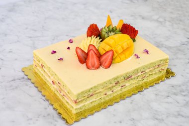 Çilek, mango, kivi ve anananas dahil olmak üzere tropikal meyveli Şam fıstıklı kek ve lezzetli tatlı kekinin narin gül yaprakları manzarası.