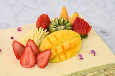 Çilek, mango, kivi ve ananas da dahil olmak üzere tropikal meyveli, zarif Pistachio Katmanı Keki ve lezzetli tatlı kekinin yakın görüntüsü.