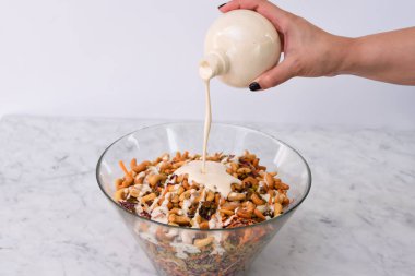 Üzerine cam kâse kremalı soslu canlı Brokoli Kaju Salatası dökülüyor, brokoli çiçekleri, kaju fıstıkları, doğranmış havuçlar ve karışık salata yanaklı kırmızı lahana manzarası yer alıyor.