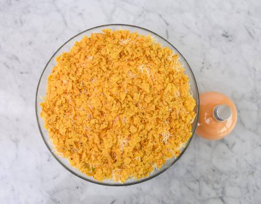 Yedi katmanlı cam bir kasede yedi katmanlı marul, mısır, kırmızı lahana, yeşil lahana, kremalı sos şişesi ve klasik ve renkli salata sosunun en üst görüntüsü olan ezilmiş patates cipsi.