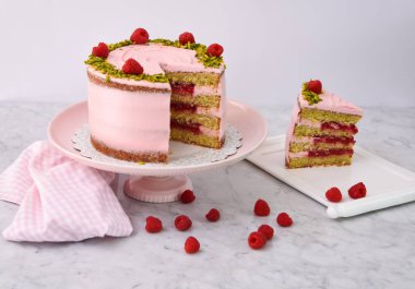 Ahudududulu Pistachio Pastası. Dilimlenmiş pembe kremalı. Taze ahududu ve doğranmış fıstıkla süslenmiş.