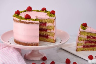 Ahudududulu Pistachio Pastası. Dilimlenmiş pembe kremalı. Taze ahududu ve doğranmış fıstıkla süslenmiş.