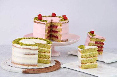 Şam fıstıklı ve ahududulu kekler ve Rose Butter kremalı dilimler, zarif tatlıların peçeteli ve beyaz kremalı.