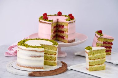 Şam fıstıklı ve ahududulu kekler ve pembe ve beyaz kremalı dilimler zarif tatlıların peçete tarafında.