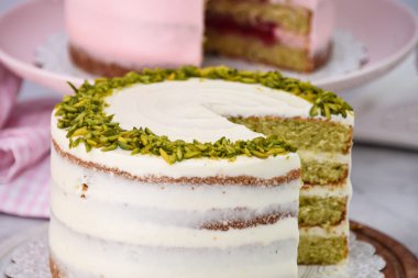 Şam fıstıklı ve ahududulu kekler ve gül yağı kremalı dilimler, peçeteye pembe ve beyaz şekerlemeler zarif tatlıların yan görüntüsü.