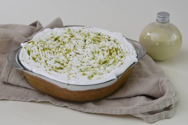 Temiz cam bir kabın içinde limonlu turta üzerine beyaz krema ve parlak yeşil limon lezzeti peçete tarafından izole edilmiş küçük süt sosu şişesi ve ferahlatıcı taze bir ikram.