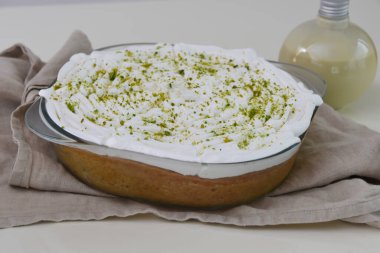 Limonlu turta şeffaf bir cam kabın içinde, üzerinde krema ve parlak yeşil limon tadı ve peçeteye izole edilmiş küçük süt sosu şişesi var.