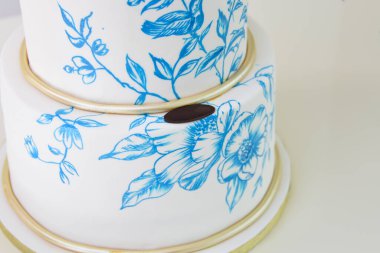 İki katlı düğün pastası, pürüzsüz beyaz kremalı. Karmaşık mavi ve beyaz çiçeklerle süslenmiş. Büyük olay pastasına yakın plan.