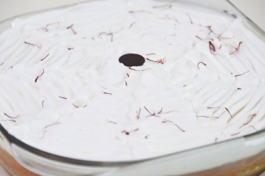 Beyaz krem şantili ve parlak kırmızı safran iplikçiklerle süslenmiş cam bir fırında safran sütlü kek aromatik sütlü keklerin yakın görüntüsü.