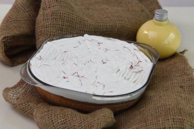 Beyaz kremayla kaplanmış, şeffaf cam bir fırında Saffron Milk Cake ve aromatik sütlü keklerin kahverengi peçete tarafında kırmızı safran ipliklerle süslenmiş.