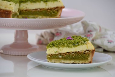 Lezzetli Pistachio Cheesecake dilimi beyaz bir tabakta sunuluyor ince yer fıstıkları ve mor çiçek yapraklarıyla kaplı zarif bir tatlıya yakın