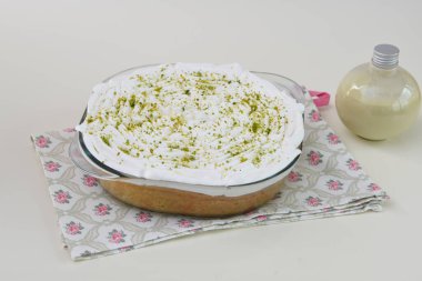 Krem şantili, şeffaf bir cam kabın içinde limonlu turta ve peçeteye izole edilmiş parlak yeşil limon tadı ve klasik tatlı sosu manzarası.