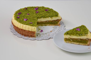 Lezzetli Pistachio Cheesecake beyaz bir tabakta sunulan dilimlenmiş fıstıklı ve mor çiçek yapraklı zarif tatlı manzaralı
