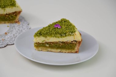 Lezzetli Pistachio Cheesecake dilimi beyaz bir tabakta sunuluyor ince yer fıstıkları ve mor çiçek yaprakları ile kaplı zarif tatlı manzarası