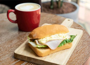 Savory Smoked Jambon, Yumurta Salatası, Marul Focaccia tahtanın üzerinde, kahvaltının yanında kahve manzaralı.