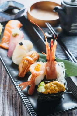 Somon, deniz kestanesi, deniz kestanesi ve karidesli nigiri ve Japon kuzeninin siyah tepsi manzaralı sashimi tabağı.