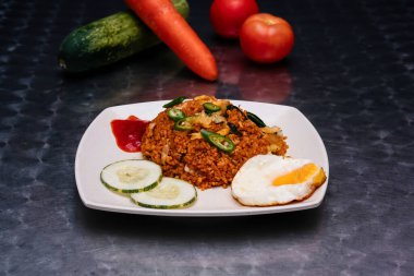 Baharatlı tavuk Nasi Goreng, kızarmış yumurta, salatalık dilimleri, ve acı sos, Malezya yemeğinin koyu arka planında izole edilmiş.