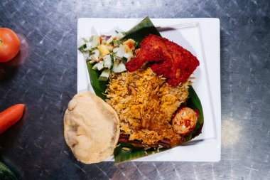 Baharatlı, yumurtalı tavuk biryanisine sos dökülüyor. Beyaz tabakta, Hint baharatının arka planında izole edilmiş.