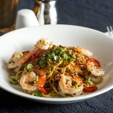 Baharatlı karides ve deniz mahsulü Aglio ve Olio taze kırmızı biber dilimleri, doğranmış yeşil soğan ve tabakta yakın plan İtalyan yemeği.