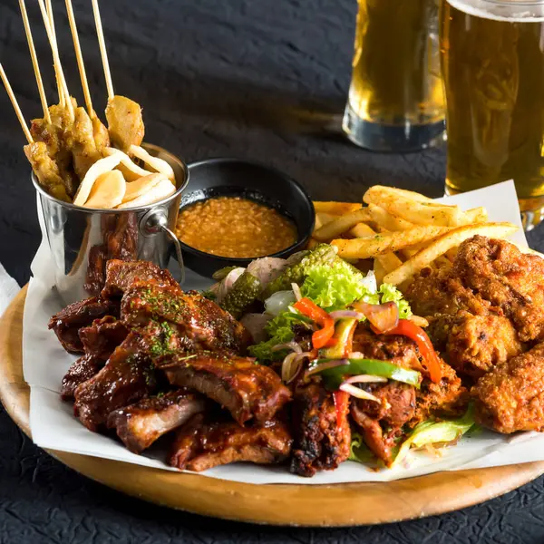 BBQ kaburga, kızarmış tavuk, satay şiş, patates kızartması, sosis ve fast food 'a yakın salata manzaralı destansı bir etobur tabağı.